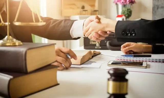 Avvocati si stringono la mano, simboli di giustizia e libri. La domanda "quanto guadagna un avvocato" è al centro di questo accordo.