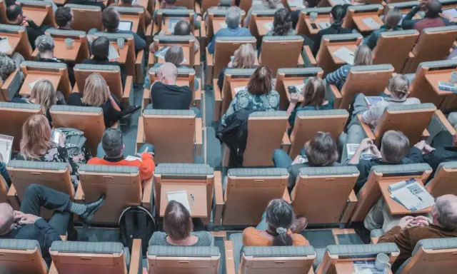 Un pubblico attento in un'aula, molti con quaderni e penne, pronti per nuovi concorsi non scaduti.