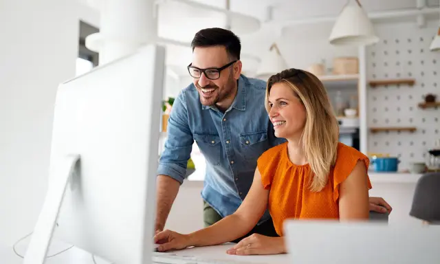 Coppia sorridente davanti al computer, forse scoprendo come funziona la banca ore per ottimizzare il lavoro.