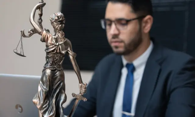 Statua della Giustizia e un uomo in giacca e cravatta, pronto per concorsi per laureati in giurisprudenza.