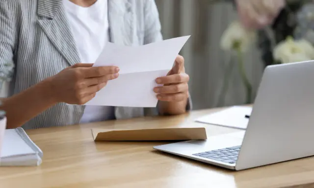 Persona esamina un documento, forse una busta paga contratto a chiamata, seduta alla scrivania con un laptop aperto.