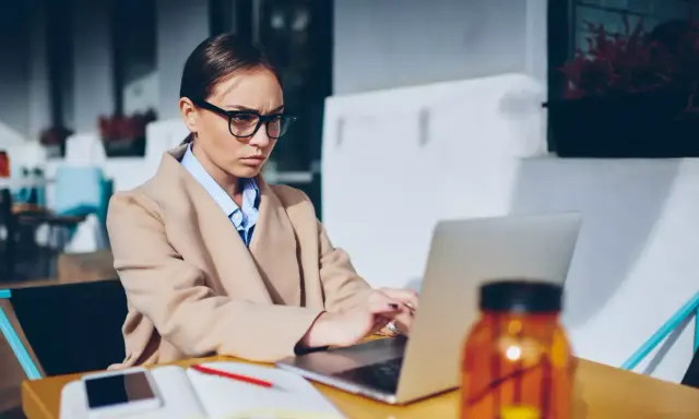 Donna con occhiali lavora al laptop, pensierosa sul gender pay gap in Italia.