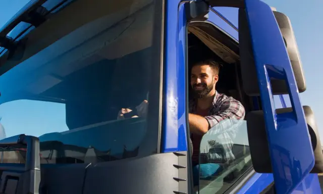 Un camionista sorridente al volante, pronto per un nuovo viaggio. Il suo stipendio camionista è meritato per il duro lavoro su strada.