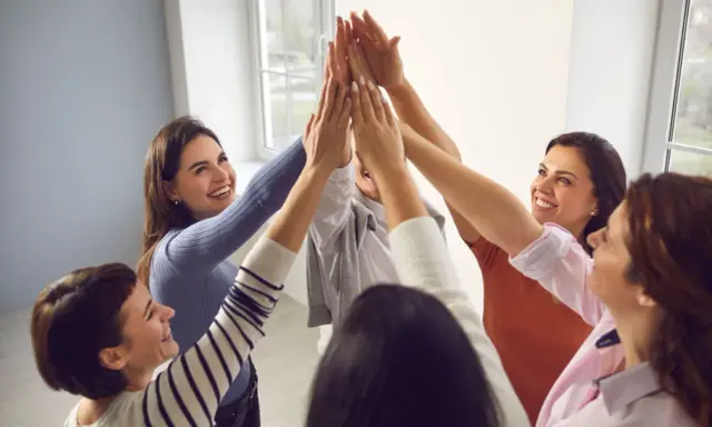 Un gruppo di donne sorridenti celebra il successo con un "high five" collettivo, simbolo di **empowerment femminile** e unione.