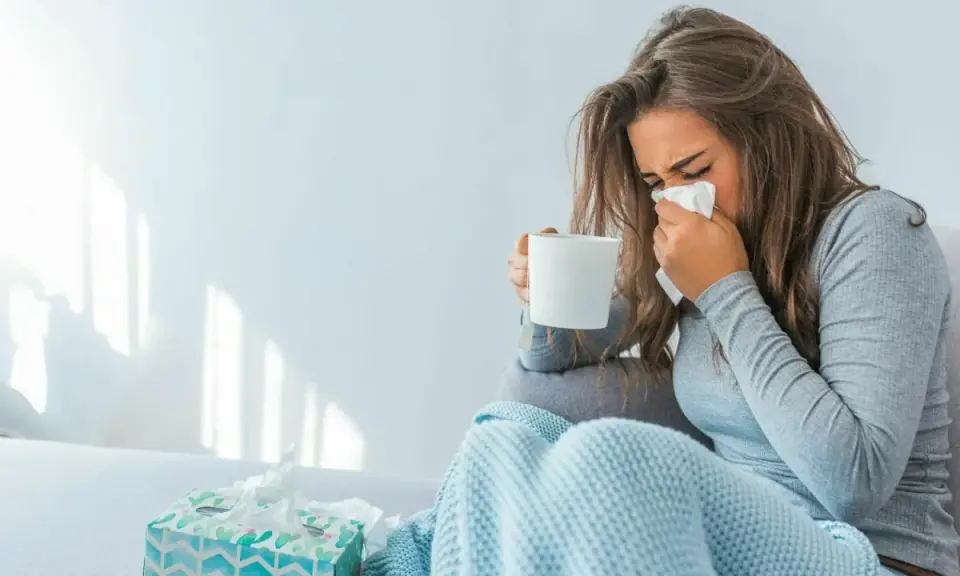 Donna con fazzoletto e tazza, coperta da un plaid. Il suo tirocinio è interrotto da una malattia.
