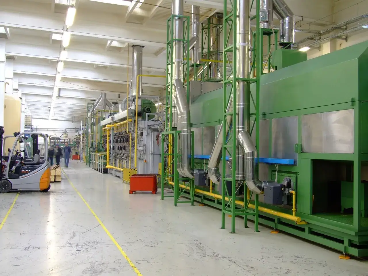 Il plant manager supervisiona un impianto industriale con macchinari verdi e tubature gialle.