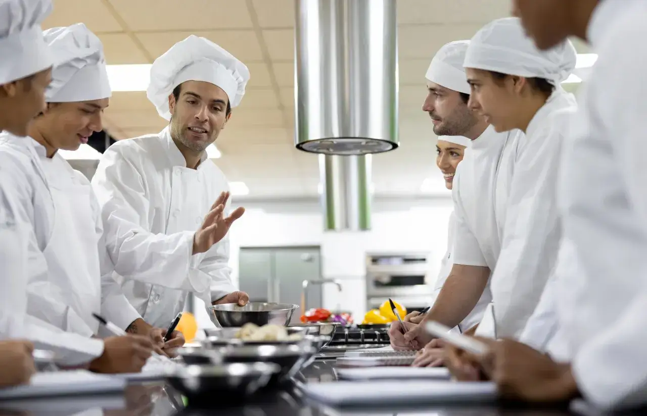 Un cuoco spiega il significato di commis di cucina a studenti in una classe pratica.