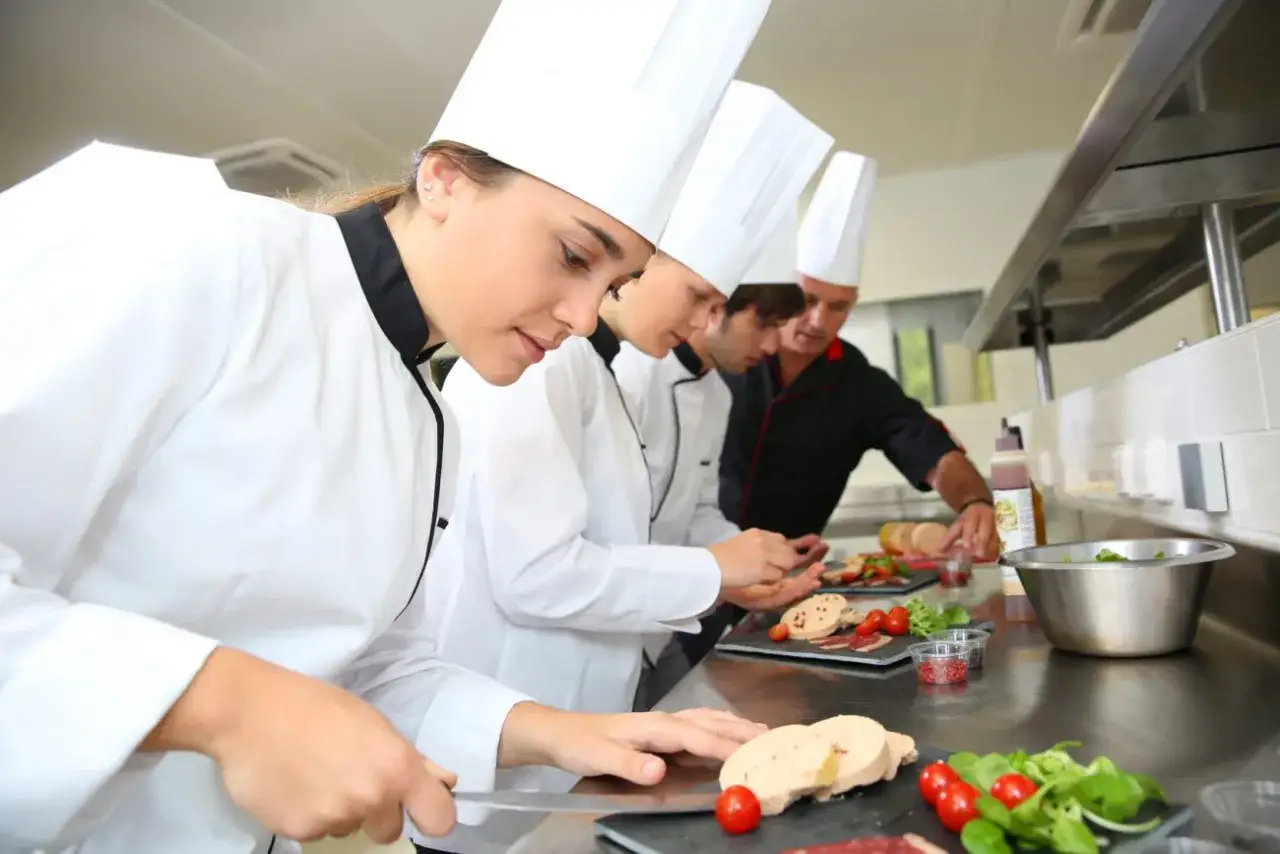 Giovani chef imparano da su chef chi è un maestro in cucina, preparando piatti raffinati con ingredienti freschi.