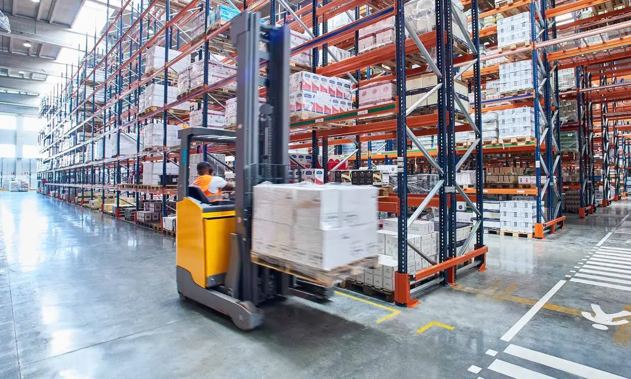 Un magazziniere con transpallet solleva scatole in un magazzino pieno di scaffalature.