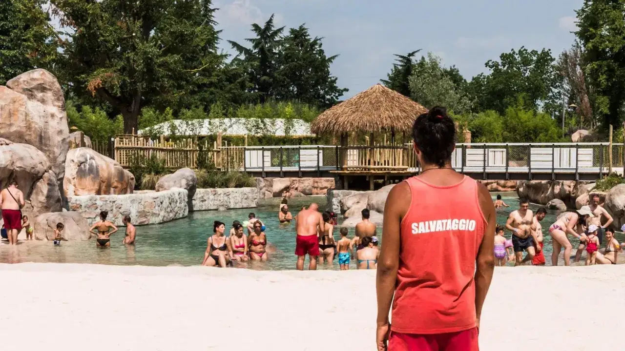 Bagnino in divisa rossa sorveglia la piscina con bagnanti. Chissà quanto guadagna un bagnino per questo lavoro estivo.