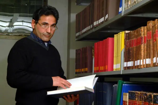 Uomo con occhiali in biblioteca, sfoglia un libro. Forse pensa al suo bibliotecario stipendio.